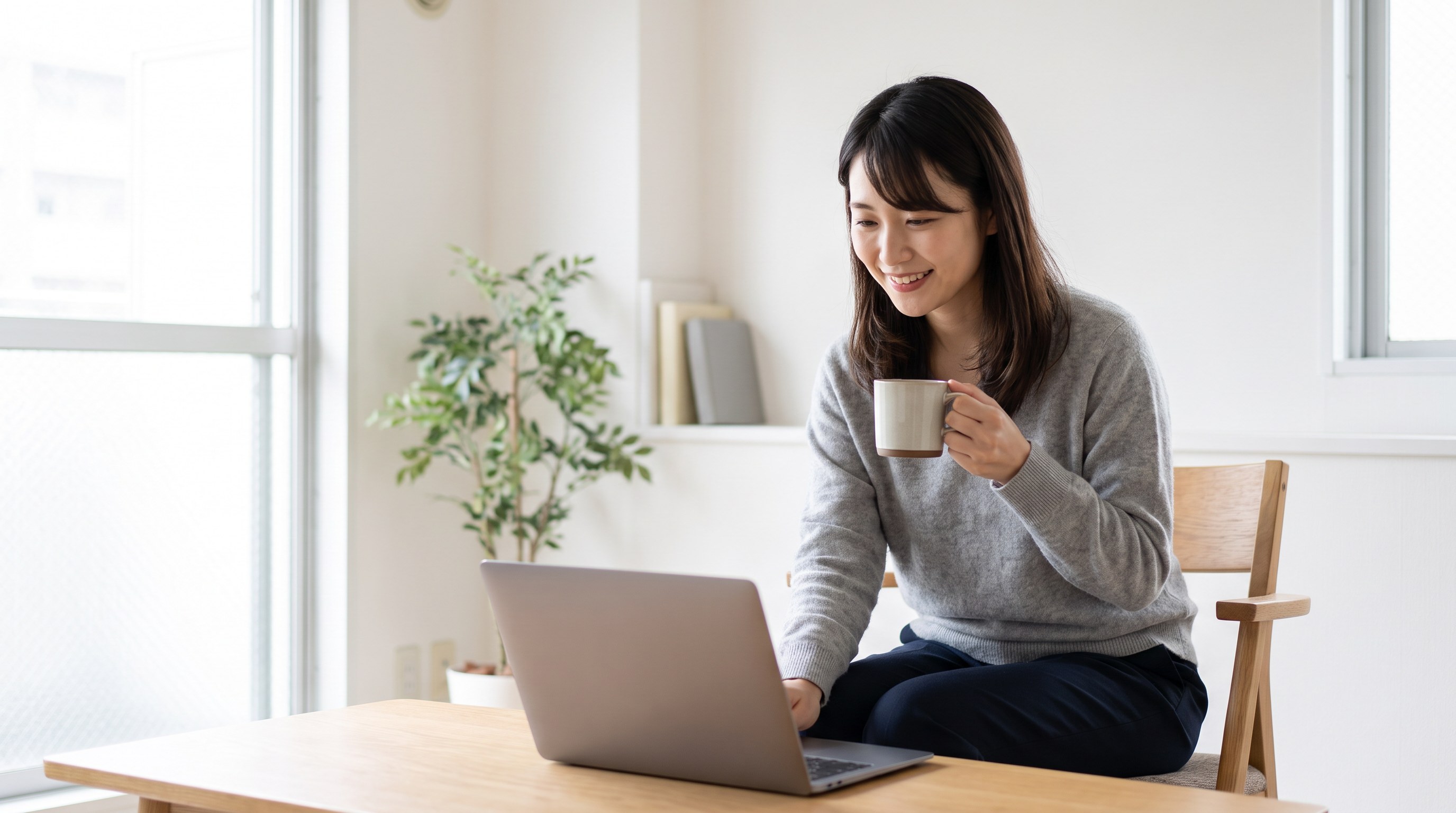 A candid three-quarter view of someone smiling while looking at a laptop, holding a mug